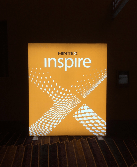 Ein beleuchtetes Nintex-Schild mit dem Wort „inspire“ darauf, das arbeitsinspirierte Werte präsentiert.