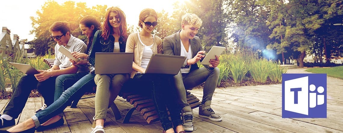 Eine Gruppe von Menschen, die Microsoft Teams nutzen, eine chatbasierte Bildungsplattform, sitzt mit Laptops auf einer Bank.